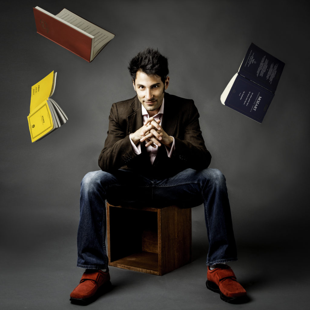 Isaac Selya seated with open orchestral scores suspended in the air around him